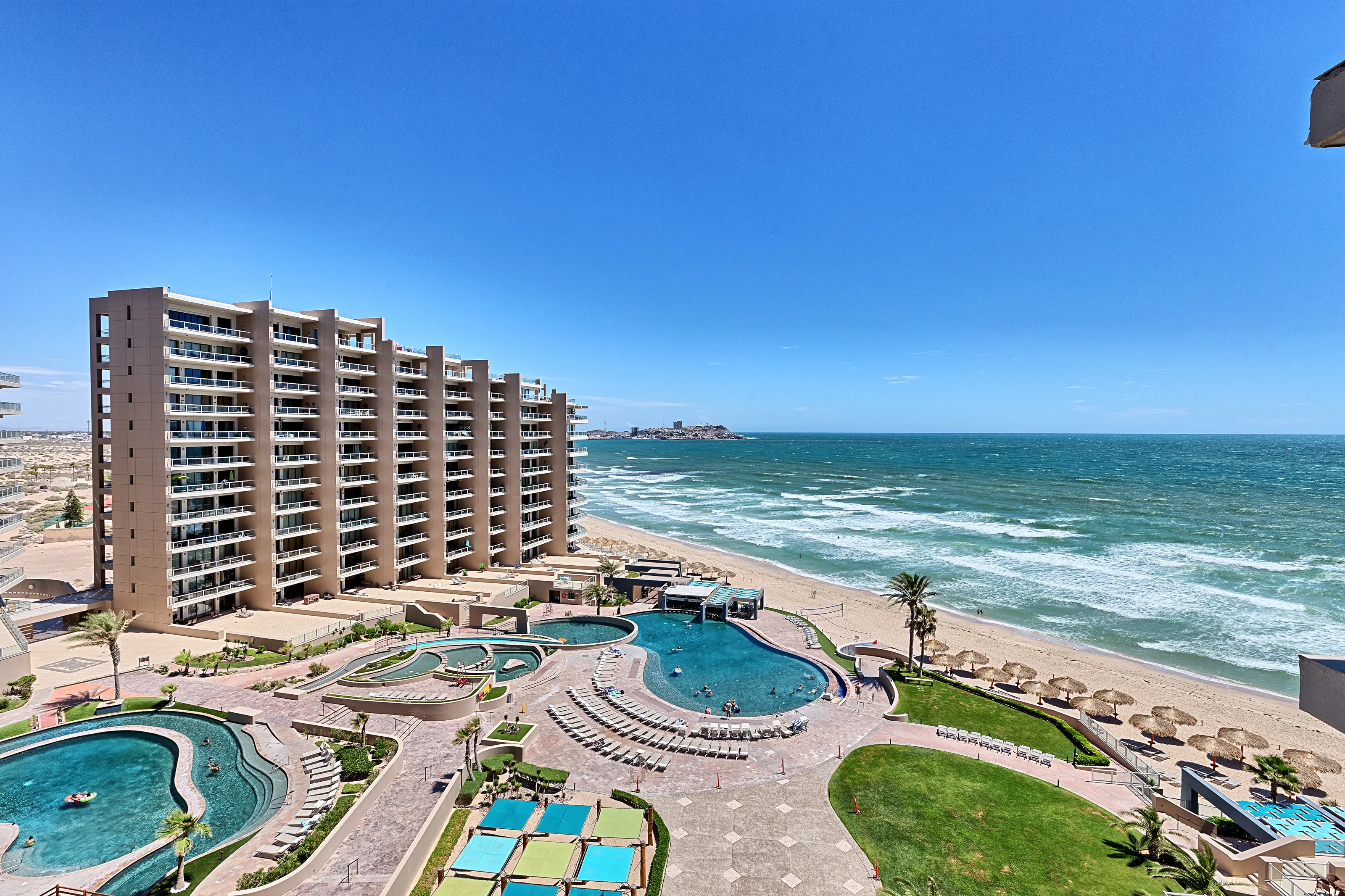 Oceanfront resort with pool and clear blue skies.