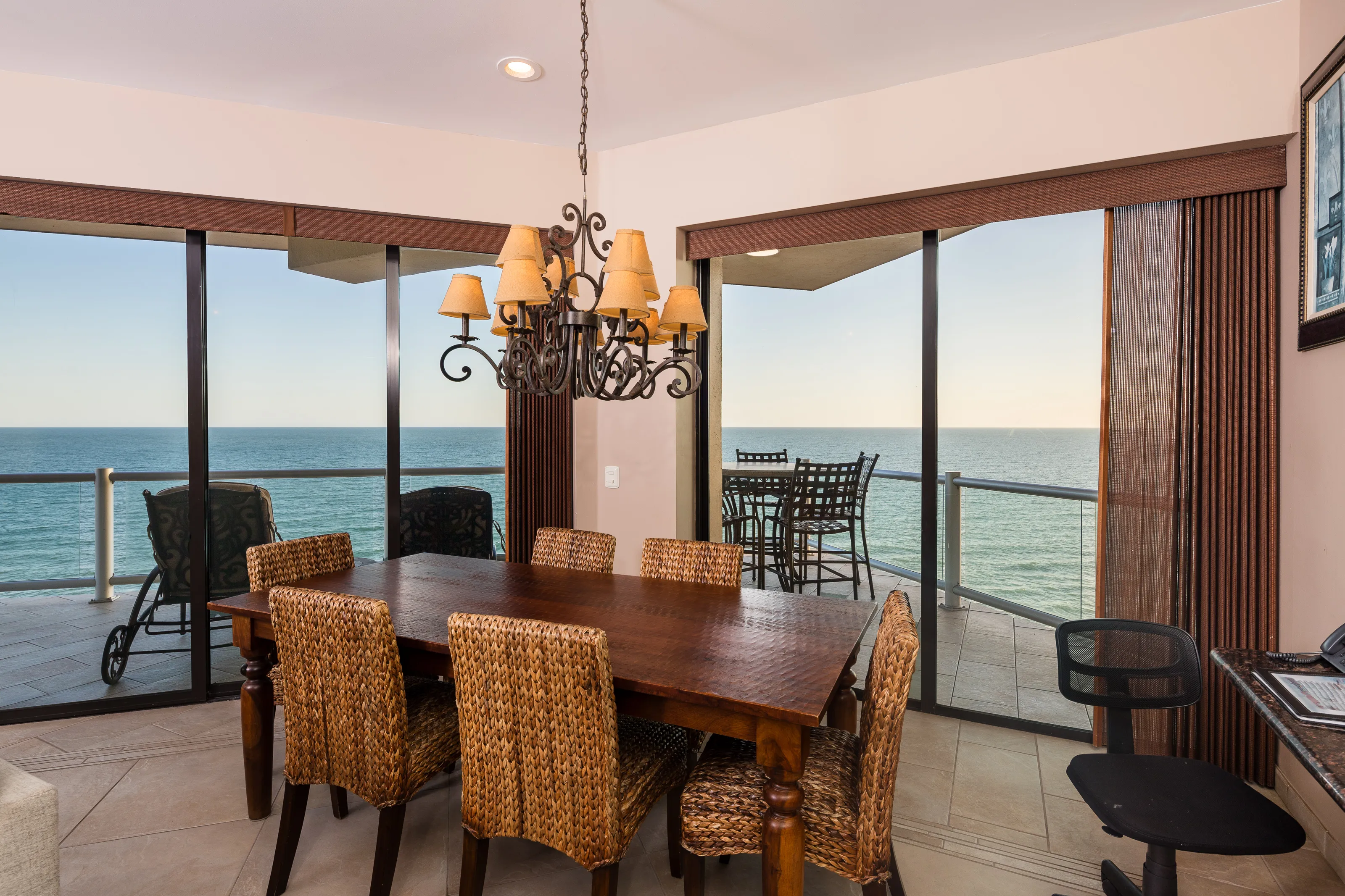 Dining area with wicker chairs and ocean view through sliding doors.